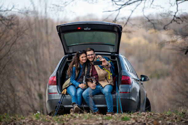 istock Young couple taking a selfie while sitting on their car trunk 1388047850