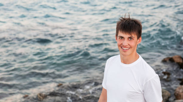 Smiling young man with braces on teeth. Caucasian man looks happily on blue sea background. Horizontal banner with copy space. stock photo