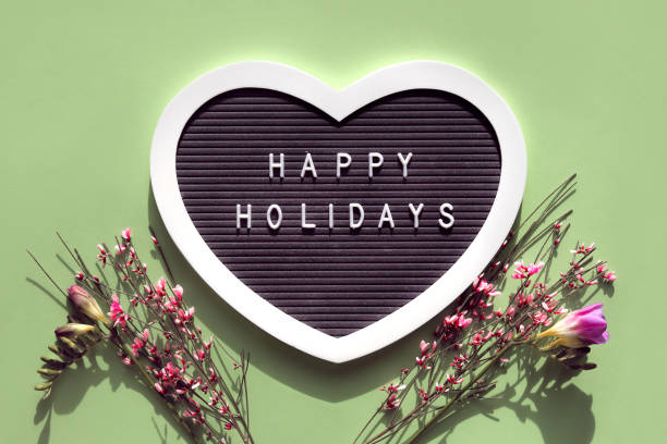 istock Happy Holidays text on felt heart shaped letter board, letterboard. Spring flat lay on light green. Pink flowers 1388050151