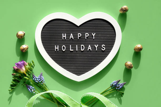 istock Happy Holidays text on felt heart shaped letter board, letterboard. Spring flat lay on light green. Pink flowers 1388050160
