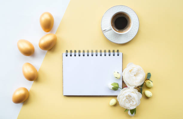 istock Golden easter eggs, coffee mug, delicate flowers and notebook with place for text on on yellow background. Trendy flat lay. minimal concept. 1388052495