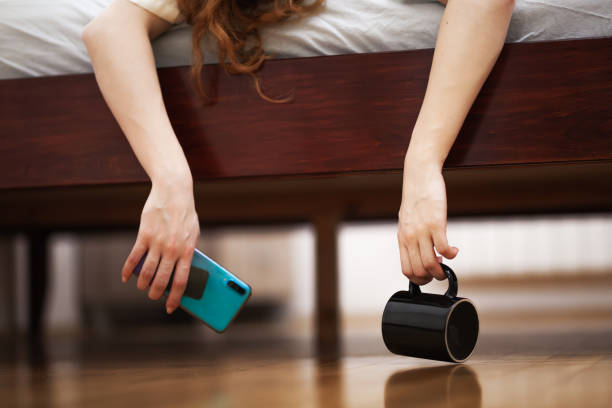 istock Female hands hanging from a beg in a begroom, holging phone and empty black cup. 1388054868