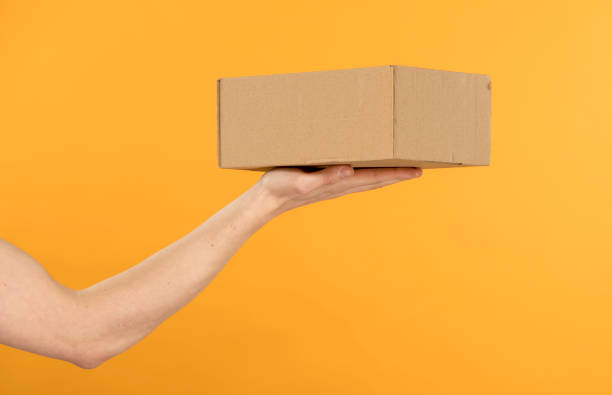 a box without inscriptions in a man's hand gives a box on a yellow bright background close-up stock photo