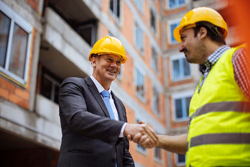 An investor and construction worker shaking hands while standing in a construction site