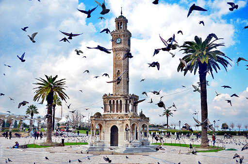 zmir, Turkey - august 11, 2010: Doves flying near historical clock tower, it was built in 1901 and accepted as the symbol of Izmir City. Konak Square with walking ordinary people