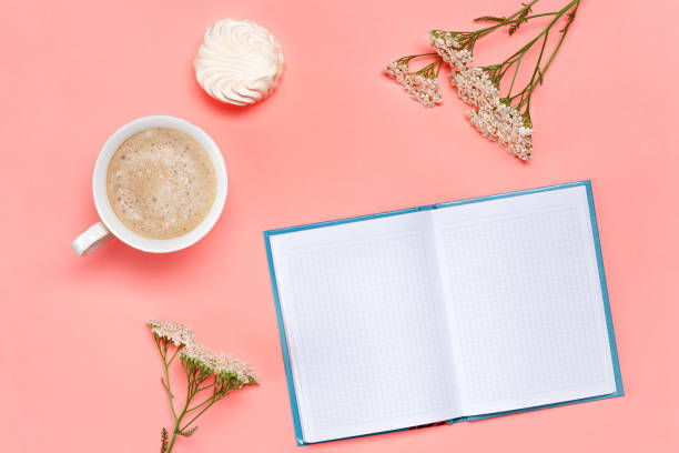 istock Top view of working desk with mock up blank notebook, coffee cup, marshmallow and flowers on pink background. 1388067928