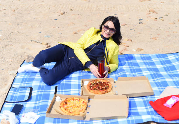 donna russa di 45 anni che va a mangiare la pizza mentre è seduta sulla spiaggia - russian ethnicity cold relaxation nature foto e immagini stock
