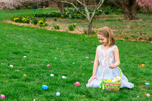 A young girl is kneeling in the grass at an Easter egg hunt