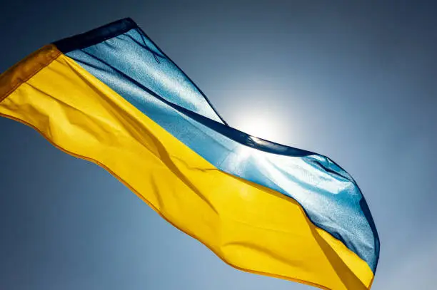 National flag of Ukraine waving outside on a wing facing the bright sky and the Sun