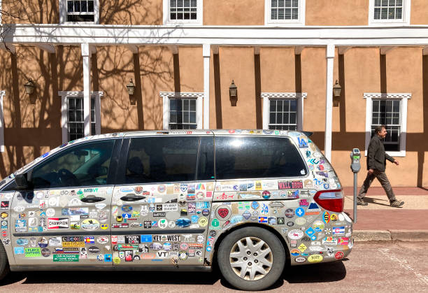 Santa Fe, NM: A man in downtown Santa Fe walks by a parked mini-van covered with bumper stickers from various US cities, states, and national parks.