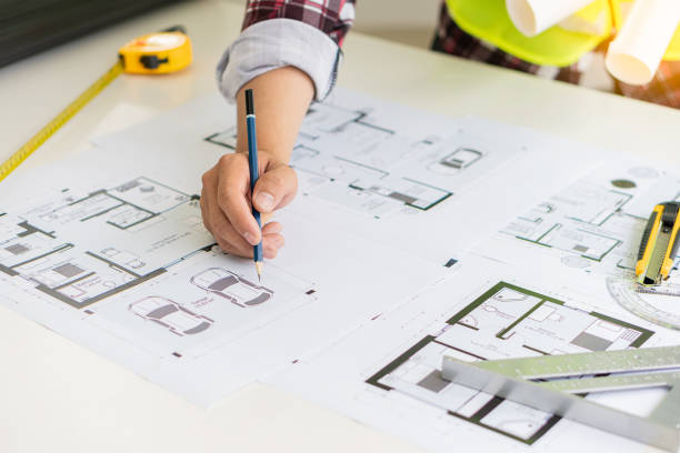 istock Young engineers and architects design, plan, measure the layout of blueprints with tabletop tools in construction concepts with hats and houses on the table. 1388078483