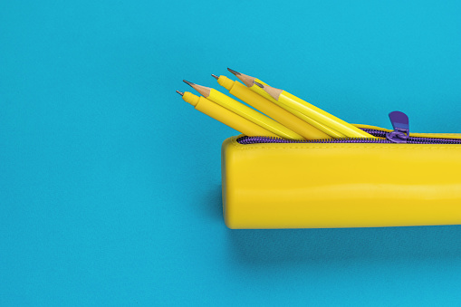 An open yellow pencil case with pens and pencils on a blue background. The minimum concept of storing school supplies. Flat lay.