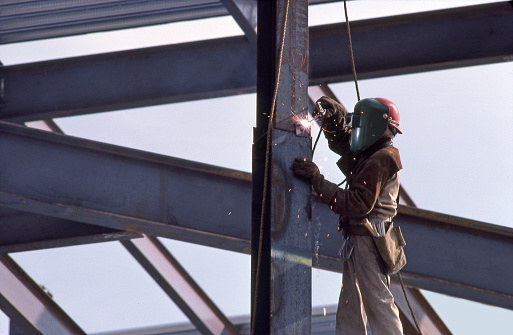 San Diego, California, USA - February 27, 2022: Sparks fly as an iron worker welds an i beam on a high rise building.