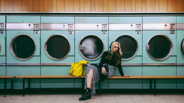 4k video footage of a young woman waiting for her laundry to be washed at a laundromat
