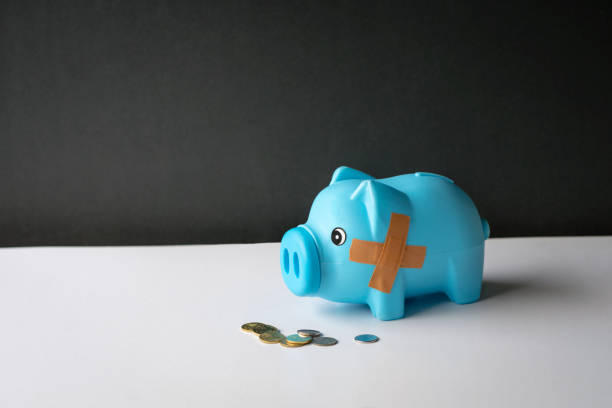 壊れた貯金箱にはバンドエイドの包帯とテーブル上のコインが付いています。 - piggy bank healthcare and medicine wound currency ストックフォトと画像