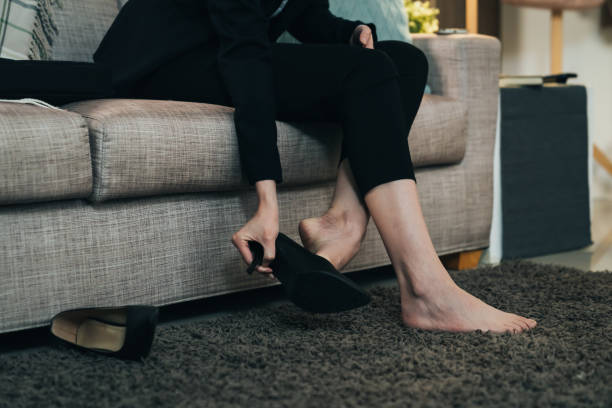 vista de cerca de una mujer de negocios que se quita el tacón alto después del trabajo en casa. mujer quitándose los zapatos descansando descalza para mayor comodidad. - undressing fotografías e imágenes de stock