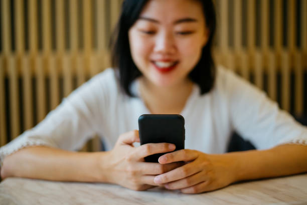 istock Smiling Asian woman using smartphone in cafe 1388096477