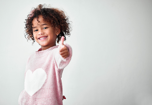 Curly blond hair teenage girl wearing grey hoodie and white top looking at copy space and smiling. Studio shot, yellow background.