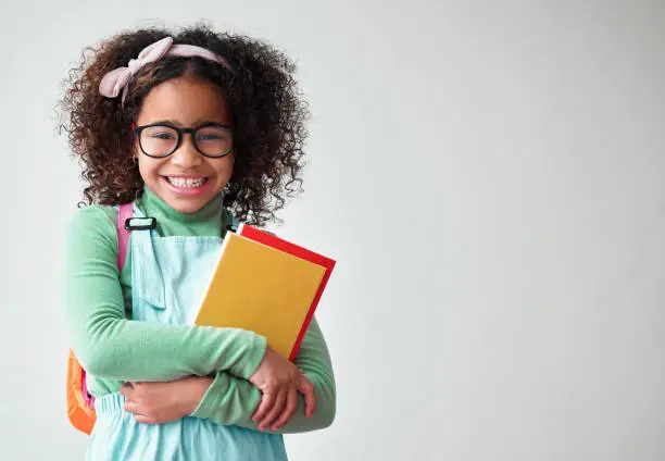 Photo of Shot of a little girl wearing glasses and holding books against a grey background