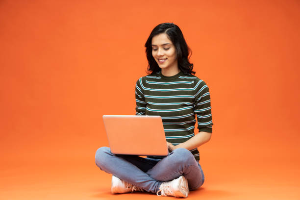 Young woman sitting on floor with laptop on orange background, stock photo stock photo