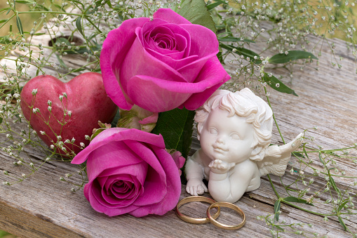 Pink rose flower arrangement with red heart and angel figurine for holidays