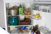 An old refrigerator with dirty dishes pots cups groceries