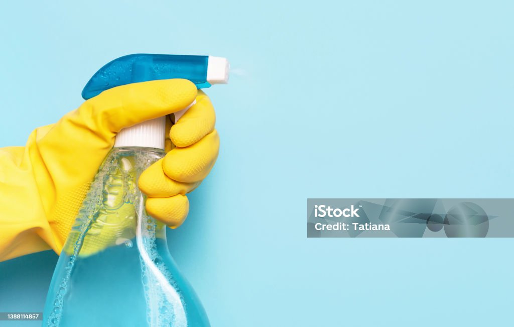 Female hand in glove holds window spray on blue background, spring cleaning concept. Female hand in glove holds window spray on blue background, a spring cleaning concept. Cleaning Product Stock Photo