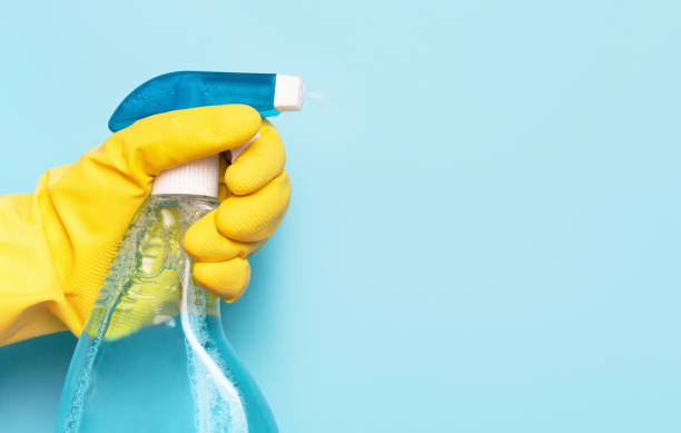 kobieca ręka w rękawiczce trzyma spray do okien na niebieskim tle, koncepcja wiosennego czyszczenia. - cleaning fluid zdjęcia i obrazy z banku zdjęć