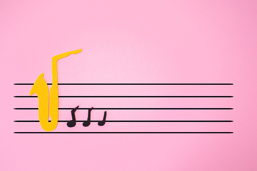 International Jazz Day. Silhouette of a saxophone cutted out of felt with notes, on a pink background in the form of a sheet of music. Flat lay.