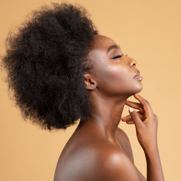 gesichtsprofil der afrikanischen schönheitsfrau, die gesicht und hals massiert. dunkles hautmodell mit afro frisur seitenansicht über beige. frauen gesichts- und körperpflege spa kosmetik - afro stock-fotos und bilder