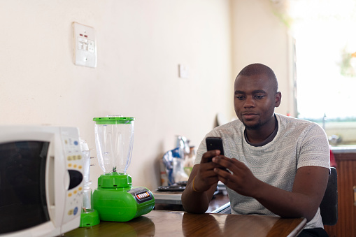 Father using mobile app to buy insurance in kitchen of rural African home