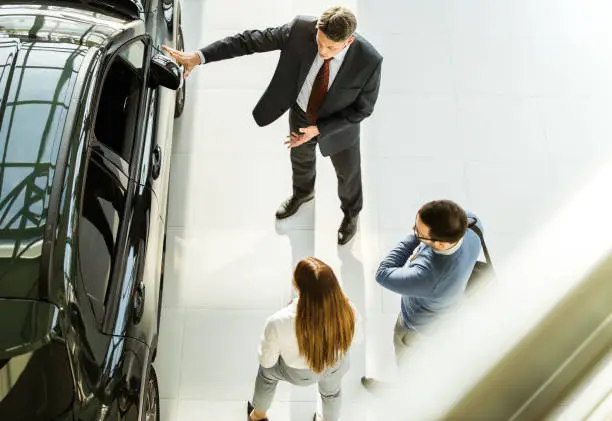 High angle view of happy mid adult salesperson talking to young couple in a car showroom. Copy space.