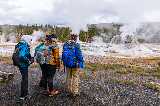 Wyoming, USA - October 1, 2019: Group of tourist on hot zone inside Yellowstone national park to watch white smoke from eruption of geysers on natural trail.