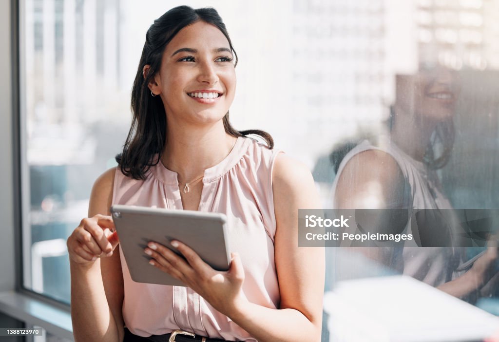 Shot of an attractive young businesswoman standing alone in the office and looking contemplative while using a digital tablet My goals are in clear sight Women Stock Photo