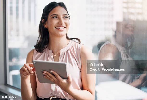 Shot Of An Attractive Young Businesswoman Standing Alone In The Office And Looking Contemplative While Using A Digital Tablet Stock Photo - Download Image Now