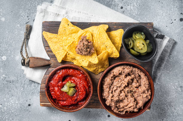 Traditional mexican refried beans with nachos, jalapeno and tomato sauce. Wooden background. Top view. Traditional mexican refried beans with nachos, jalapeno and tomato sauce. Wooden background. Top view. Refried Beans stock pictures, royalty-free photos & images