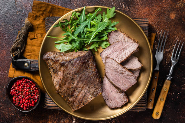 istock Roast Tri Tip or sirloin bottom beef steak on a plate with arugula. Dark background. Top view 1388127206