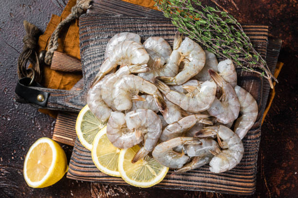 istock Raw tiger white shrimp prawn on board with herbs. Dark background. Top view 1388127612