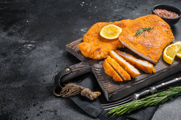 schnitzel weiner frit en tranches sur une planche de bois avec des herbes. fond noir. vue de dessus. espace de copie - wiener schnitzel photos et images de collection