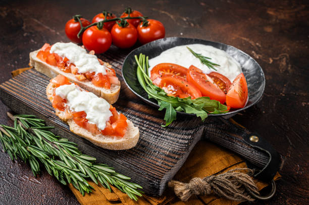 istock Bruschettas with stracciatella cheese, chopped cherry tomatoes and rosemary. Dark background. Top view 1388129364