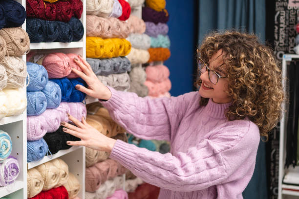 cliente femminile, scegliendo il gomitolo di lana, presso il negozio di tessuti - negozio di tessuti foto e immagini stock