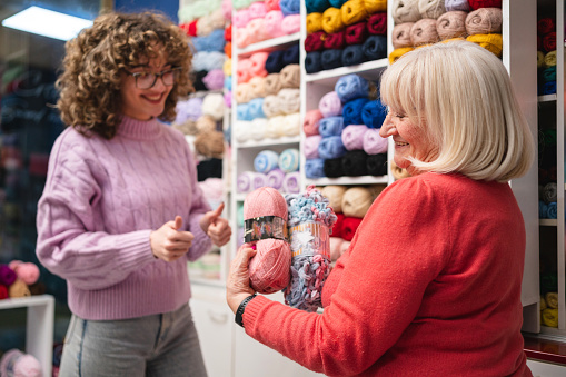 Senior Caucasian saleswoman, showing to young female customer, ball of wool