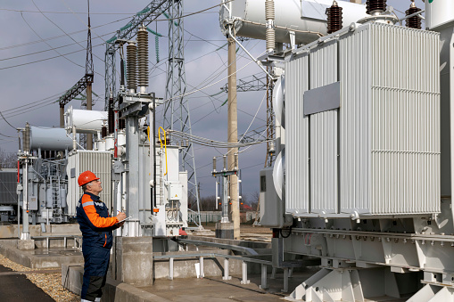 Un ingeniero eléctrico inspecciona los transformadores de potencia en las centrales eléctricas. Un ingeniero con casco rojo y mono protector. Trabajos de subestaciones photo