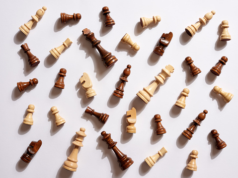 Top view of white and brown wooden chess pieces fallen on white background.