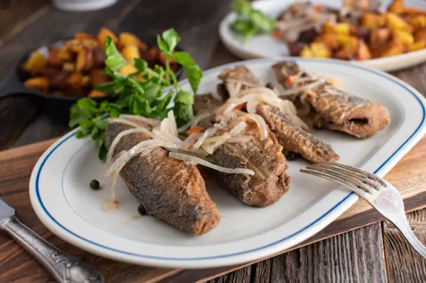 Delicious german fish dish  with with sour marinated or pickled fried herring served with fresh pan fried potatoes on rustic and wooden table background. Ready to eat