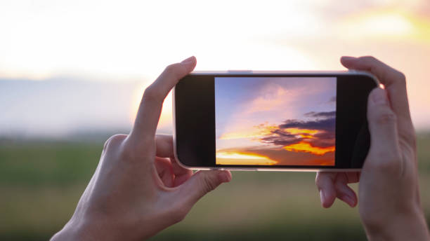 mains de femme retenant le téléphone mobile au coucher du soleil - prendre une photo photos et images de collection