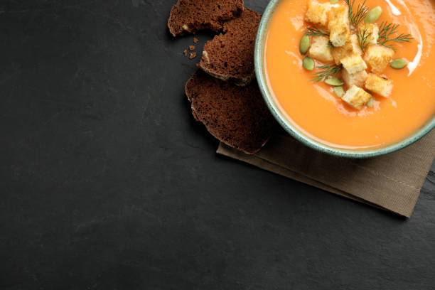istock Delicious pumpkin soup in bowl on black table, top view. Space for text 1388135487