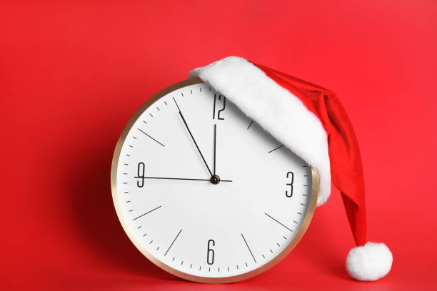 istock Clock with Santa hat showing five minutes until midnight on red background. New Year countdown 1388136157