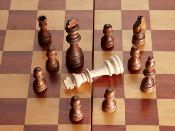 Fallen king is surrounded by the rival chess pieces.