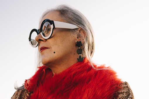 Pensive senior woman looking away while standing outdoors. Stylish elderly woman wearing colourful casual clothing and eyeglasses. Mature woman reflecting on memories of the past.